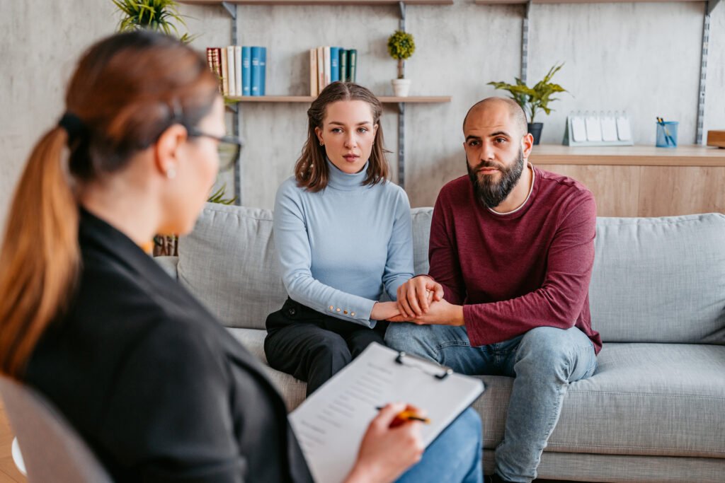 Warm, candid photo of a couple talking with a therapist in soft natural light.
